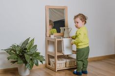 a young child standing in front of a mirror holding a potted plant and looking at it