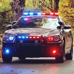 a police car with its lights on is driving down the street in front of some trees