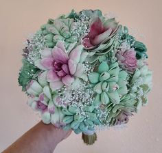 a bridal bouquet with pink and green flowers in someone's hand against a wall