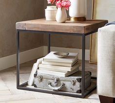 a wooden table topped with books and a white vase filled with flowers next to a chair