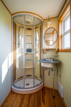 a bathroom with a stand up shower next to a white sink and wooden flooring