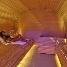 a woman laying in a wooden sauna with two benches next to her on the floor