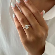 a woman's hand with a diamond ring on her left hand and white nails