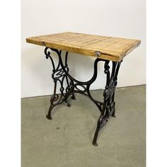 an antique sewing table with wooden top and iron legs, on cement flooring area