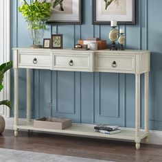 a white console table with two pictures on the wall above it and a potted plant