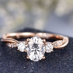 an engagement ring with three stones on it, sitting on top of a black rock