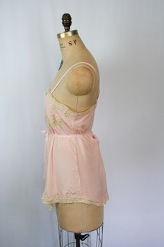 "Vintage 1920s pink silk crepe embroidered floral lace chemise Beautiful lace inset neckline with a sweet ribbon flower Pick stitch embroidery detail on front bust line and more beautiful lace Lace trimmed hem Fabric tie that is attached at back waist and can be worn tied around waist or in a simple bow at back Silk ribbon straps Crotch has been undone so it can be worn as a camisole Pull on MEASUREMENTS: taken flat Fits like a Small Bust: up to 36\" Waist: up to 38\" Hips: up to 46\" Strap Leng Pink Silk Spaghetti Strap Camisole, Pink Lace Trim Camisole In Coquette Style, Pink Lace Trim Coquette Camisole, Pink Lace Camisole In Coquette Style, Pink Lace Coquette Camisole, Pink Lace Trim Slip Dress For Daywear, Feminine Pink Silk Camisole, Vintage Lace Camisole For Spring, Vintage Lace Camisole Sleepwear