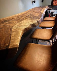 several chairs are lined up at the edge of a long wooden table with metal barstools