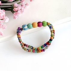 two bracelets with colorful beads are sitting next to pink flowers on a white surface