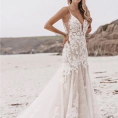 a woman standing on top of a beach wearing a white wedding dress with floral appliques