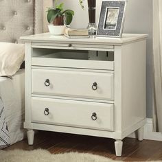 a white nightstand with two drawers and a framed picture on the top, next to a bed