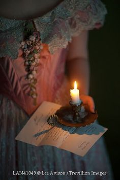 a woman in a dress holding a lit candle and an open letter with writing on it