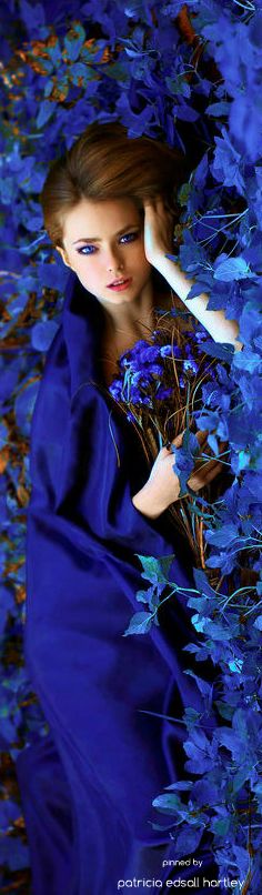 a woman in a blue dress is laying on the ground surrounded by leaves and flowers