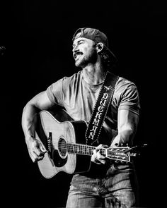 a man holding a guitar while standing in front of a microphone and wearing a hat