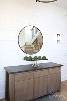 a mirror on top of a wooden dresser next to a stair case with green plants