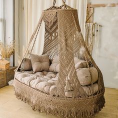 a wicker hanging bed with pillows on it in a room next to a window