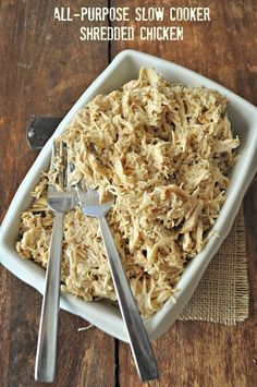 a white bowl filled with shredded chicken next to a fork and spoon on top of a wooden table