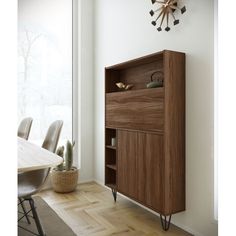 a wooden cabinet sitting in front of a window next to a table with chairs and a clock on the wall