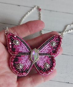 a hand holding a pink and black beaded butterfly