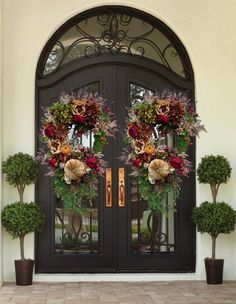 two wreaths on the front door of a house with potted plants and trees