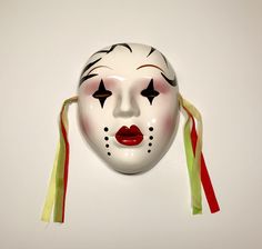 a white mask with black and red designs on it's face is hanging from a wall