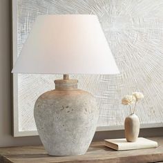 a white vase sitting on top of a wooden table next to a lamp and book