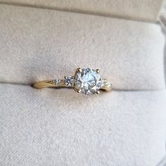 an engagement ring with three stones in it on a white cushioned surface, next to a pillow