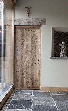 a wooden door sitting next to a window on top of a stone floor in front of a white wall