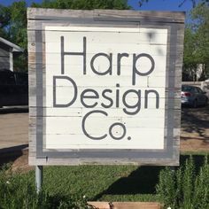 a sign that says harp design co in front of some grass and bushes with cars parked behind it