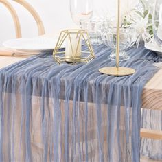 the table is set with white plates and silverware, gold candlesticks and blue sheer curtains