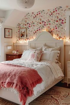 a white bed topped with pillows and blankets next to a wall covered in floral decorations