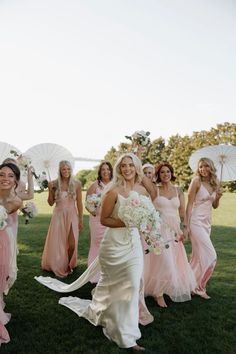 a bride and her bridal party in pink dresses with parasols on the grass