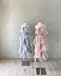 two mannequins with different colored dresses on stands in front of a wall