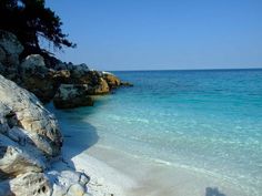 the water is crystal blue and clear with white sand on the beach near some rocks