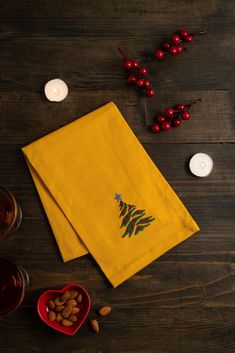 two yellow napkins sitting on top of a wooden table next to cups and candles