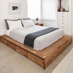 a bed sitting on top of a wooden platform next to a white dresser and window