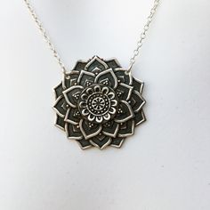 a silver necklace with a flower design on the front and center piece is hanging from a chain