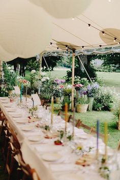 a long table set up for an outdoor event with flowers and candles on the tables