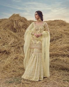 a woman standing in front of hay bales wearing a yellow dress and shawl