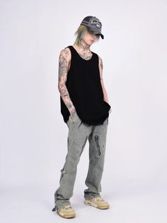 a man with tattoos standing in front of a white background wearing grey jeans and a black tank top