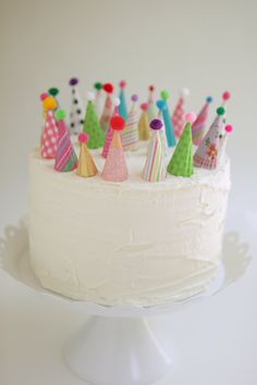 a white cake topped with lots of colorful frosting and small birthday hats on top of it