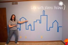 a woman standing in front of a blue wall with buildings drawn on it and writing life with more believe