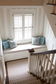 a window seat with two pillows on it in front of a white wall and stairs