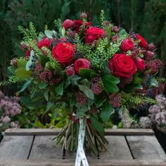 a bouquet of red roses sitting on top of a wooden table next to other flowers