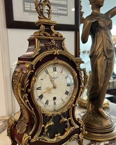 an antique clock is sitting on a marble counter top in front of a statue and framed pictures