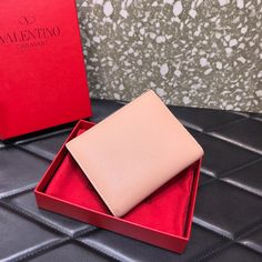 a pink wallet sitting in a red box on top of a black tile floor next to a red box