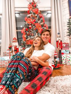 a man and woman sitting in front of a christmas tree with presents on the floor