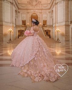 a woman in a pink wedding dress standing on the stairs at a building with chandeliers