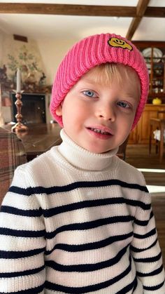 a young boy wearing a pink hat and striped sweater