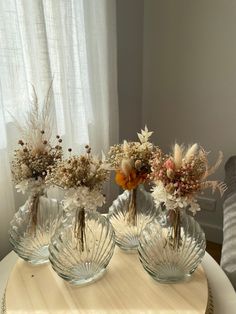 three glass vases with dried flowers in them on a table next to a window